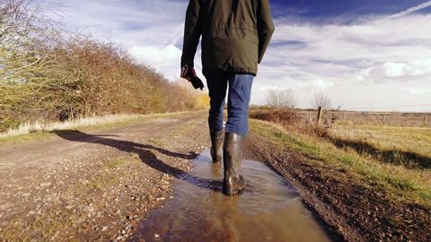 Slow motion of man walking through muddy puddles in the UK, not showing full person in the shot, only 3/4 of person.