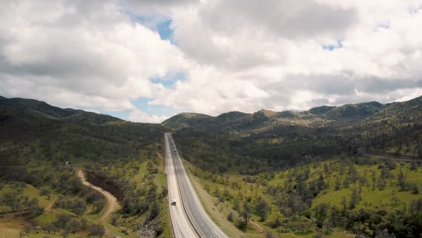 Cars driving down highway in peaceful green California mountains, AERIAL