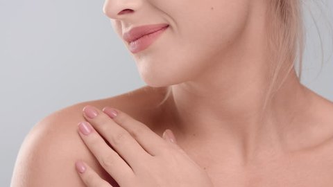 Close-up beauty portrait of young woman touching her smooth skin in collarbone area against grey background | skin care concept