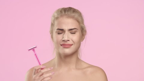 Medium close-up Beauty portrait of young blonde Caucasian woman throws out women shaver and smiling on light pink background | Laser treatment for unwanted hair concept