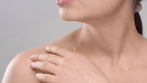 Close-up beauty portrait of young adult woman, that gently strokes her clavicles on light grey background | Skincare concept