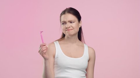 Medium close-up portrait of young brunette Caucasian woman throws out women shaver and smiling on light pink background | Laser treatment for unwanted hair concept
