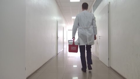 Doctor with red organ trafficking container going along the corridor towards the exit from the hospital.