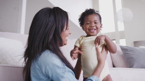 African American Mother Playing With Baby Daughter Tickling Her And Lifting Her In The Air At Home