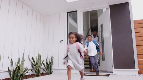 African American Excited Children Running Out Of Front Door On Way To School Watched By Father