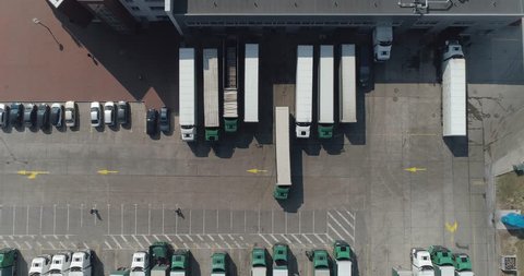 Buildings of logistics center, warehouses near the highway, truck parking process, view from height, a large number of trucks in the parking lot near warehouse.