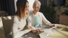 Tilt up of cheerful young woman smiling, talking and supporting senior grandmother while she surfing the Net on new digital tablet at table in home - Powered by Shutterstock - Get 15% off with code: PIKWIZARD15