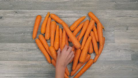 Closeup of woman's nad child's hands put carrots in the shape of a heart on a white background in fast motion. Healthy food concept: film stockowy