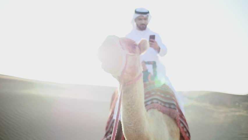 Man with traditional uae kandura clothes , riding his camel in the desert
