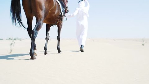 Emirates man with traditional clothes walking his horse in the desert
