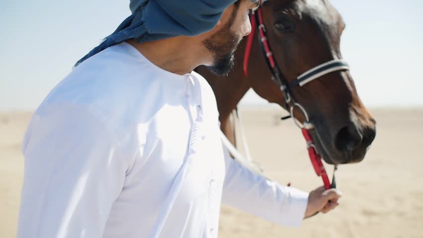 Emirates man with traditional clothes walking his horse in the desert
