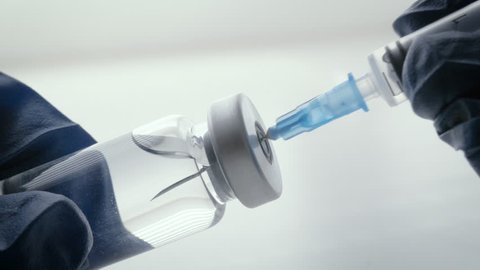 Filling syringe with mandatory vaccinations. A blue, gloved hand inserts the needle of the injection device into the rubber stopper of the vaccine vial and draws in the immunization.