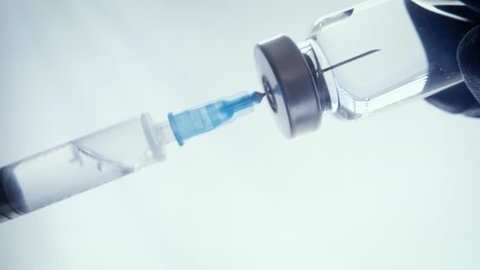 Closeup of a doctor filling a syringe with vaccines. Needle of the immunization device punctures the rubber seal of the glass vial, drawing in the medicine.