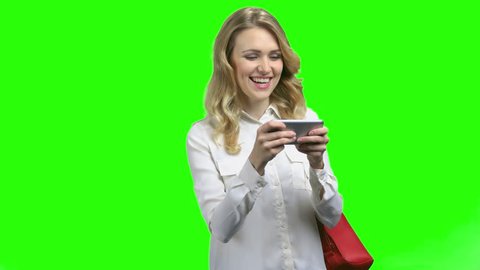 Excited woman using smartphone on green screen background. Young happy woman typing message on cell phone on Chroma Key background. People, modern technology and emotion concept.