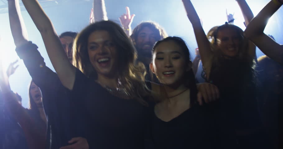 Front view close up of diverse group of people dancing at a concert in nightclub.