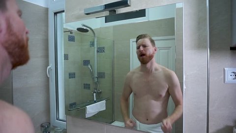 Young caucasian man doing a happy dance in the bathroom wearing white towel