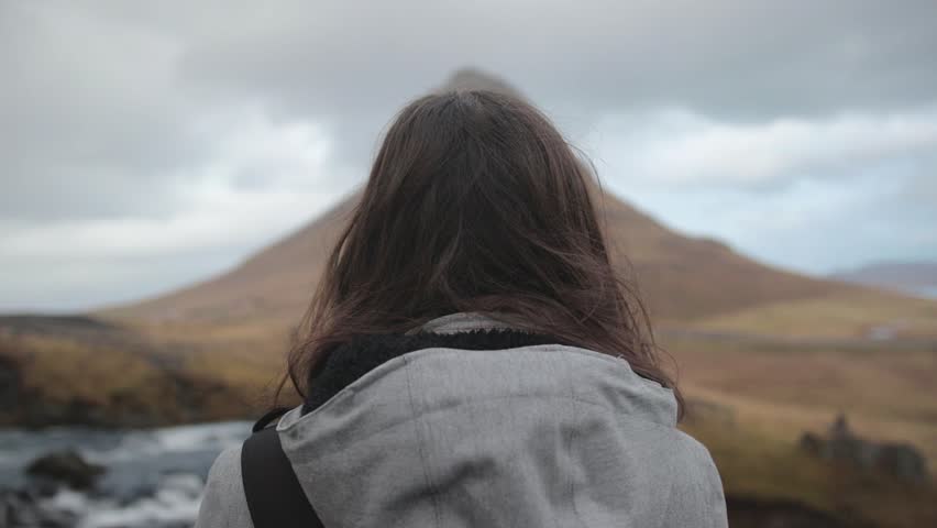 Girl stands in front of Kirkjufell, Icelandic mountain.