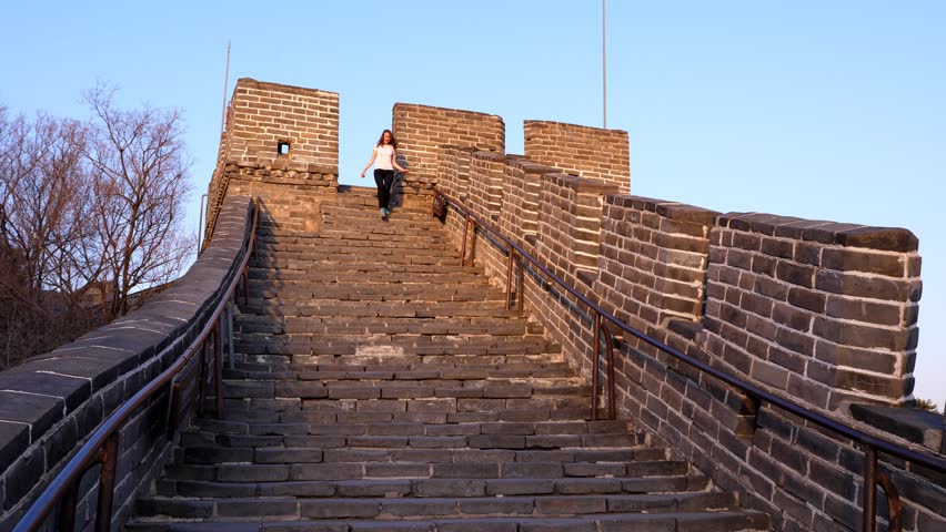 Tourist woman go downstairs at Great Wall of China, walk from watch tower by steep stairs. Old fortification at Badaling site, happy visitor pass by way down
