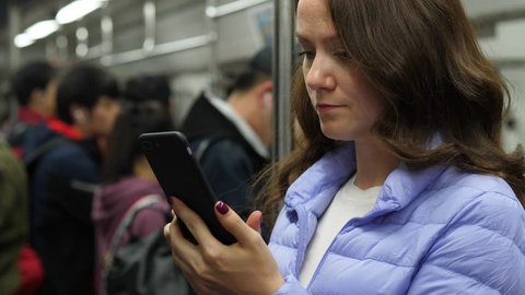 Caucasian woman using smartphone while travelling at subway in Beijing, portrait shot with blurred background. Lady focused on phone, scroll through images or watch messages