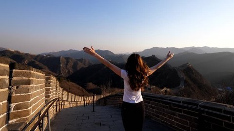 Tourist woman enjoy view at top of Great Wall of China, rise hands up in excitement, looking to Badaling from height. Beautiful scenery, old fortification lies across highland area