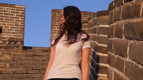 Tourist woman stand at Great Wall, look aside, low angle portrait shot at sunny evening. Long haired lady enjoy famous China landmark, Badaling section of old border fortification