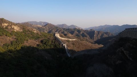 Badaling Great Wall of China at evening time, stone fortification lies on hills, large mountains seen on background. Early spring time, some green trees seen on slopes