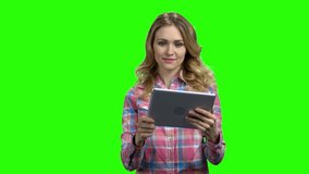 Woman having a video call on green screen. Young smiling woman holding digital tablet and waving with hand. Alpha Channel background.