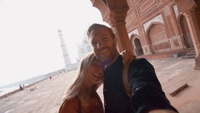 Young couple taking selfie portrait at the Taj Mahal international landmark in India- Man and woman takes selfie while traveling  having fun discovering and sightseeing 