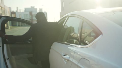 At sunset african american man opens the door of a white car and sits behind the wheel young vehicle open passenger arm auto street automobile businessman buy jacket close up slow motion