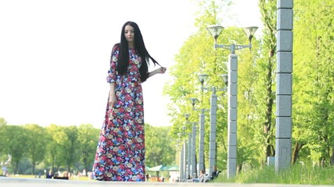 Young girl model brunette walking in the park. The beautiful long dress. Close median overall plans. The beautiful nature and the beauty of the girl.