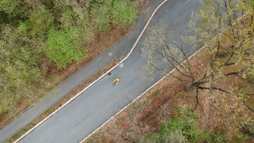 Aerial view of girl in raincoat ride bicycle in the rainy park. Cyclist woman riding bicycle in the park