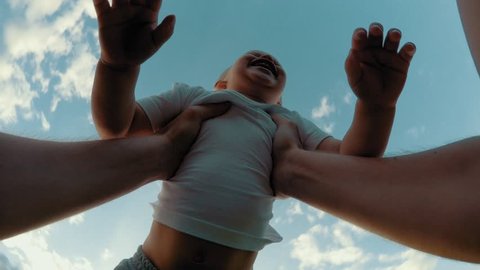 Hands of carefree father rising up and spinning little cute smiling son sky in background POV shot low angle close-up happy child boy playing with dad enjoying having good time outdoor