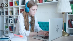 Beautiful teen girl preparing for exam using laptop at the library, wearing earphones