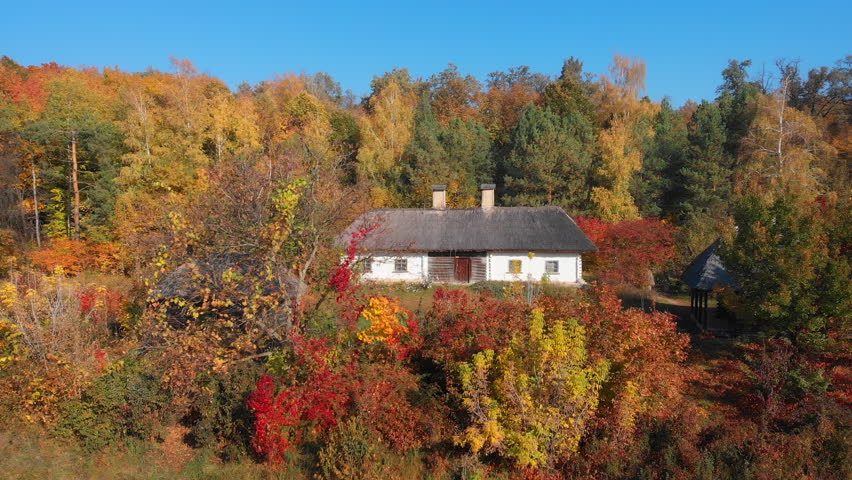Traditional house with thatched roof and two chimneys stands amongst the changing autumn leaves in this rural. Ukrainian village. Video 4k