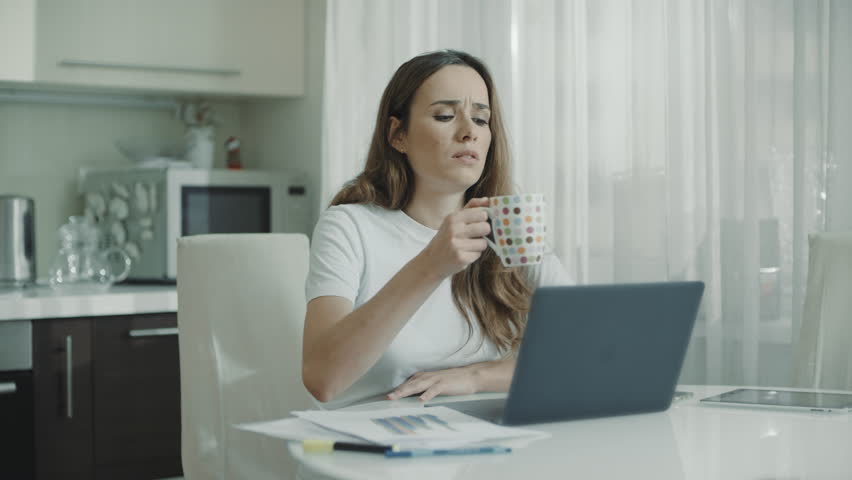 Tired woman using laptop computer at home. Close up of serious woman drinking tea cup on kitchen. Adult student studying online on notebook. Female professional reading news on laptop | Shutterstock HD Video #1027710659