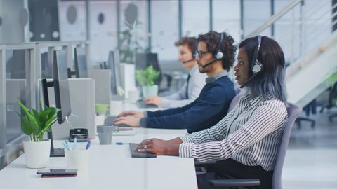 Team of Handsome and Beautiful Diverse Multicultural Customer Service Operators Working at a Busy Modern Call Center with Specialists Wearing Headsets and Actively Taking Calls.