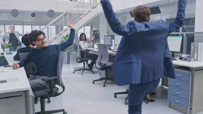 Young Happy Business Manager Wearing a Suit and Tie Dancing and Giving High Fives in the Office. Celebrating Success. Diverse and Motivated Business People Work on Computers in Modern Open Office. Royalty-Free Stock Footage #1027712564