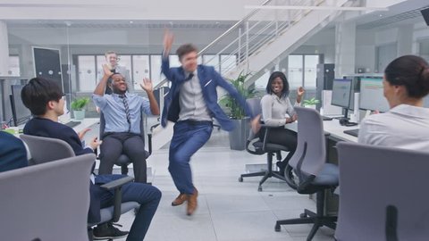 Young Happy Business Manager Wearing a Suit and Tie Dancing and Giving High Fives in the Office. Celebrating Success. Diverse and Motivated Business People Work on Computers in Modern Open Office.