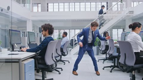 Young Cheerful Handsome Business Manager Wearing a Suit and Tie Dancing in the Office. Dances Like Robot. Diverse and Motivated Business People Work on Computers in Modern Open Office.