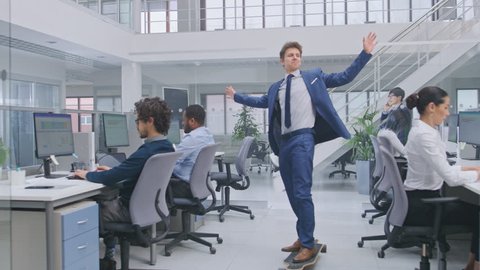 Young Happy Handsome Manager Wearing a Suit and Tie Rides a Longboard. Diverse and Motivated Business People Work on Computers in Modern Open Office.