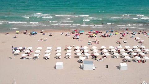 Aerial footage of the beach umbrellas and surf board rental at Alicante Beach,ing sideways