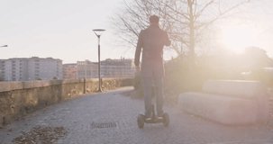 Business man riding personal transporter in city commuting to work or home while calling using smartphone. Modern future transport technology. Sidewalk urban outdoor.Warm sunset backlight.4k slow motion 60p video
