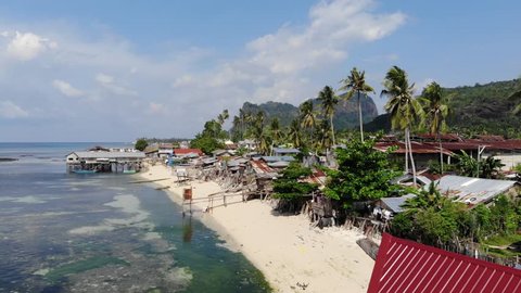Drone ascending and backing away from the beach and buildings along the shore of Tawi Tawi. Storm damaged homes of old wood and metal roofs. Third world poverty seen from the air in paradise.
