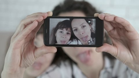 Funny selfie. A woman with a child is grimacing. Mother and daughter are photographed on a smartphone.