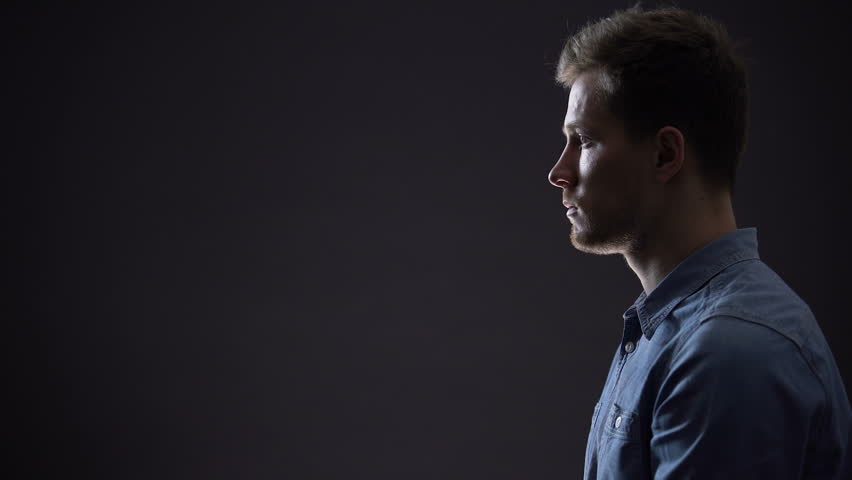 Handsome young man showing silence gesture, mysterious secret, side view