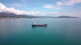 Aerial footage of tanker ships on water in sunny day, wide angle view. Beautiful mountains and blue sky on background