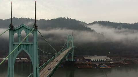 Beautiful drone view of St Johns Bridge, drone flying slightly above the side of the bridge, mountains, trees and foggy background. Portland, Oregon.