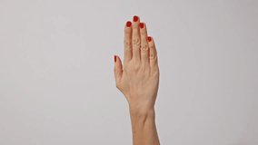 Beautiful young woman's hands with bright red manicure, one hand gently massaging the other, isolated on gray background. 4k video footage.