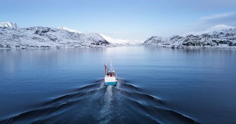 Amazing aerial drone follow shot of traditional fishing boat heading out towards the open ocean on a beautiful cold winter day in the Arctic Circle, Scandinavia, northern Europe