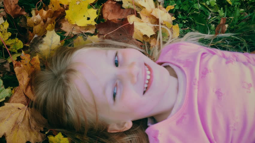 A happy young girl making leaf angels in slow motion, filmed in UHD 4K
